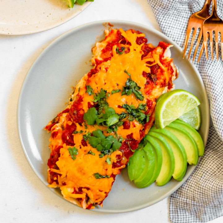 Close-up of a lightened-up chicken enchilada being served, showing the creamy sauce layer, shredded chicken filling, and melted cheese with fresh cilantro garnish