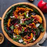lighter autumn harvest salad with massaged kale, roasted butternut squash, farro, apple, and pomegranate arils in a wide wooden bowl with maple-dijon vinaigrette