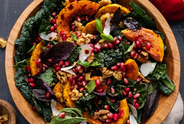 lighter autumn harvest salad with massaged kale, roasted butternut squash, farro, apple, and pomegranate arils in a wide wooden bowl with maple-dijon vinaigrette