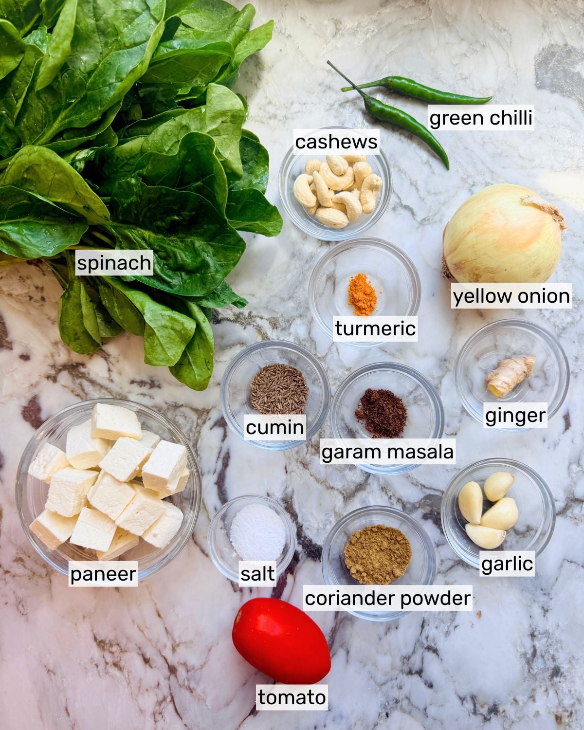 Step-by-step ingredients flat lay for Palak Paneer showing fresh spinach, paneer cubes, whole spices, ginger, garlic, and onion on a marble surface
