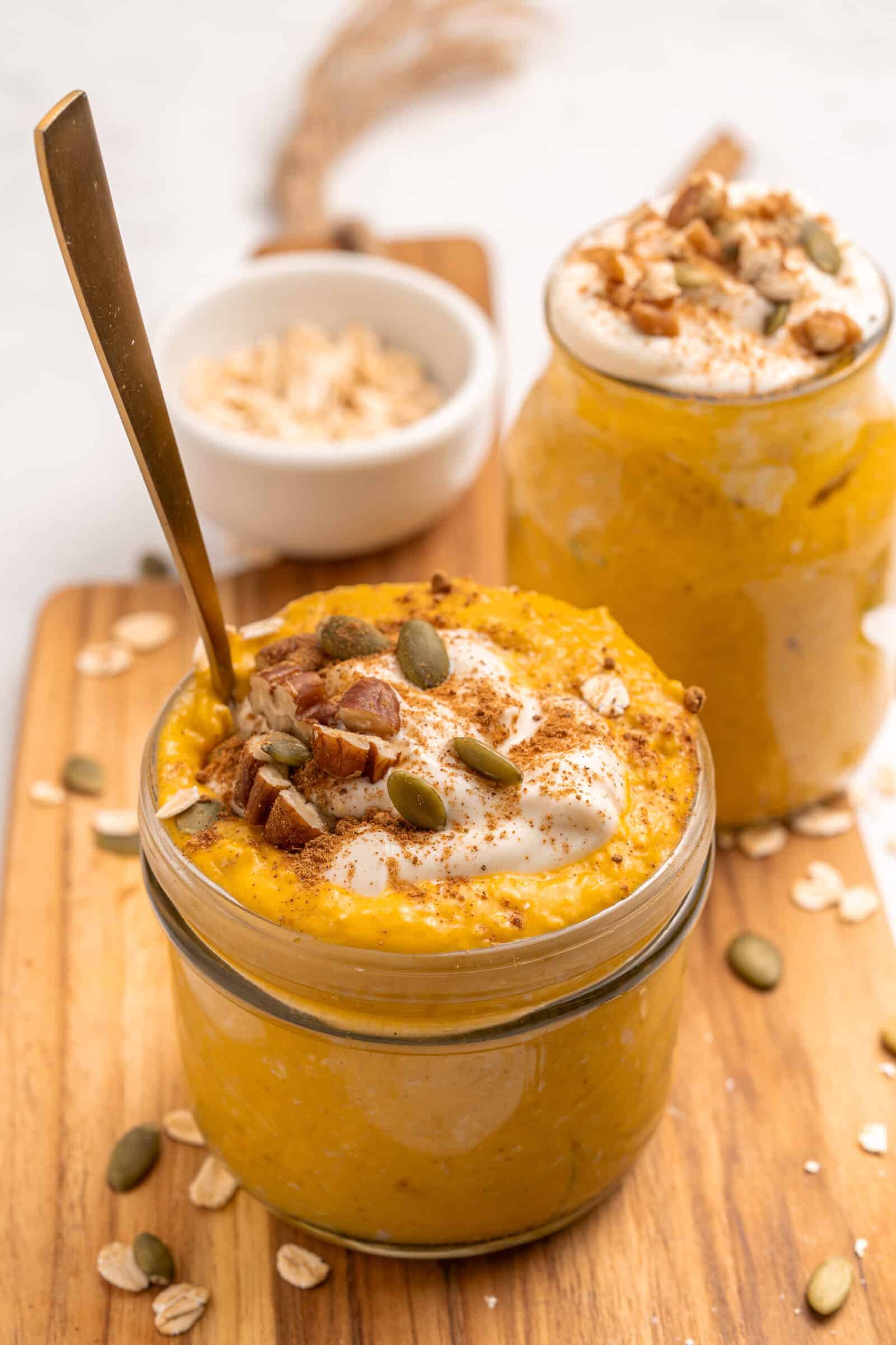 Close-up of a spoonful of pumpkin spice overnight oats being lifted from a glass jar, showing the creamy layered texture with visible oats, pumpkin swirls, and a sprinkle of cinnamon on top