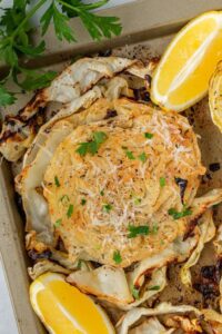Roasted cabbage steaks on a sheet pan with crispy golden edges, drizzled with olive oil and garnished with fresh parsley