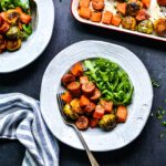 Close-up of sliced turkey sausage and caramelized fall vegetables on a white plate, garnished with fresh parsley and a wedge of lemon
