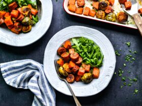 Close-up of sliced turkey sausage and caramelized fall vegetables on a white plate, garnished with fresh parsley and a wedge of lemon