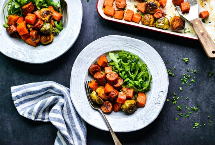 Close-up of sliced turkey sausage and caramelized fall vegetables on a white plate, garnished with fresh parsley and a wedge of lemon