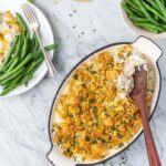 Slow cooker million dollar chicken casserole served in a white bowl topped with golden buttery Ritz cracker crumble, garnished with fresh parsley, shot on a warm wooden table