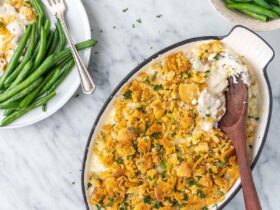 Slow cooker million dollar chicken casserole served in a white bowl topped with golden buttery Ritz cracker crumble, garnished with fresh parsley, shot on a warm wooden table
