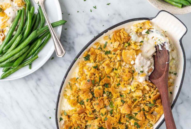 Slow cooker million dollar chicken casserole served in a white bowl topped with golden buttery Ritz cracker crumble, garnished with fresh parsley, shot on a warm wooden table