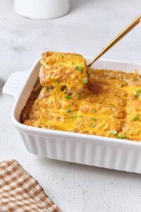 Golden tater tot casserole fresh from the oven in a white baking dish, with crispy tots on top and melted cheese bubbling at the edges, styled on a rustic wooden table
