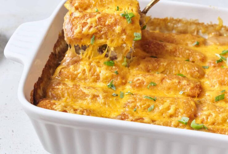 Golden tater tot casserole fresh from the oven in a white baking dish, with crispy tots on top and melted cheese bubbling at the edges, styled on a rustic wooden table