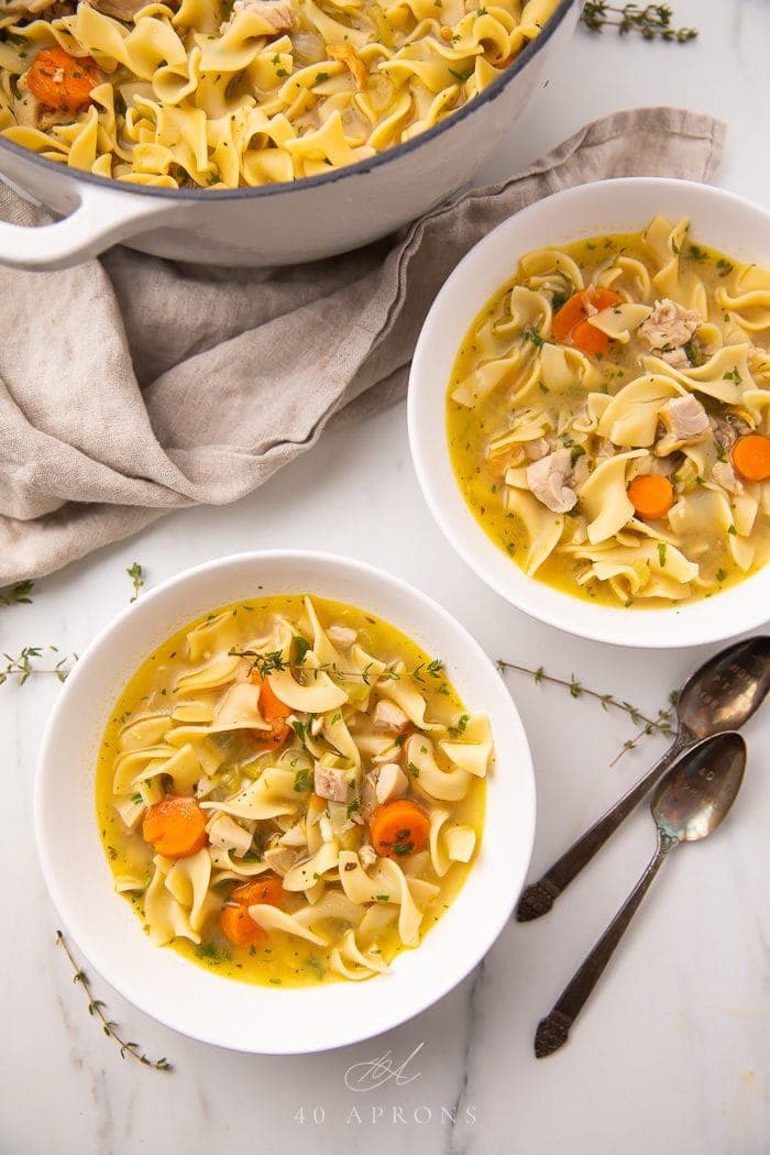 A steaming bowl of turkey noodle soup with egg noodles, sliced carrots, shredded turkey, and fresh parsley on a rustic wooden table