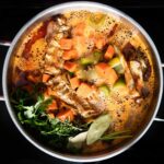 Turkey carcass simmering in a large stockpot with onion, celery, carrots, and fresh herbs for homemade broth