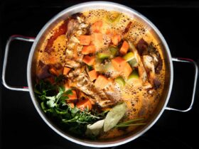 Turkey carcass simmering in a large stockpot with onion, celery, carrots, and fresh herbs for homemade broth