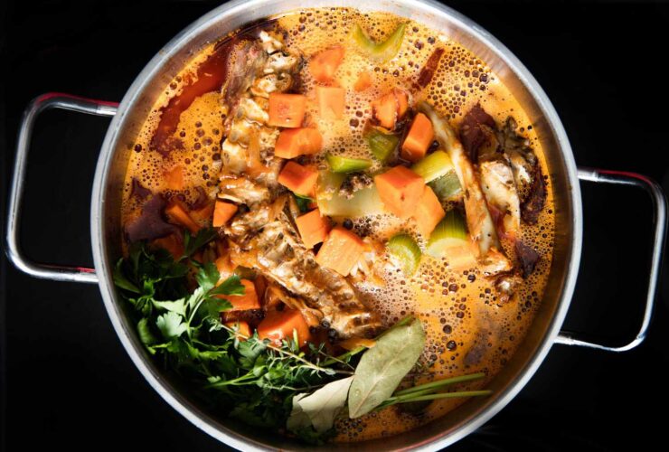 Turkey carcass simmering in a large stockpot with onion, celery, carrots, and fresh herbs for homemade broth